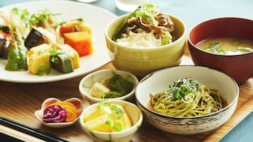 A variety of dishes including noodles, vegetables, and soup, served on a wooden table.