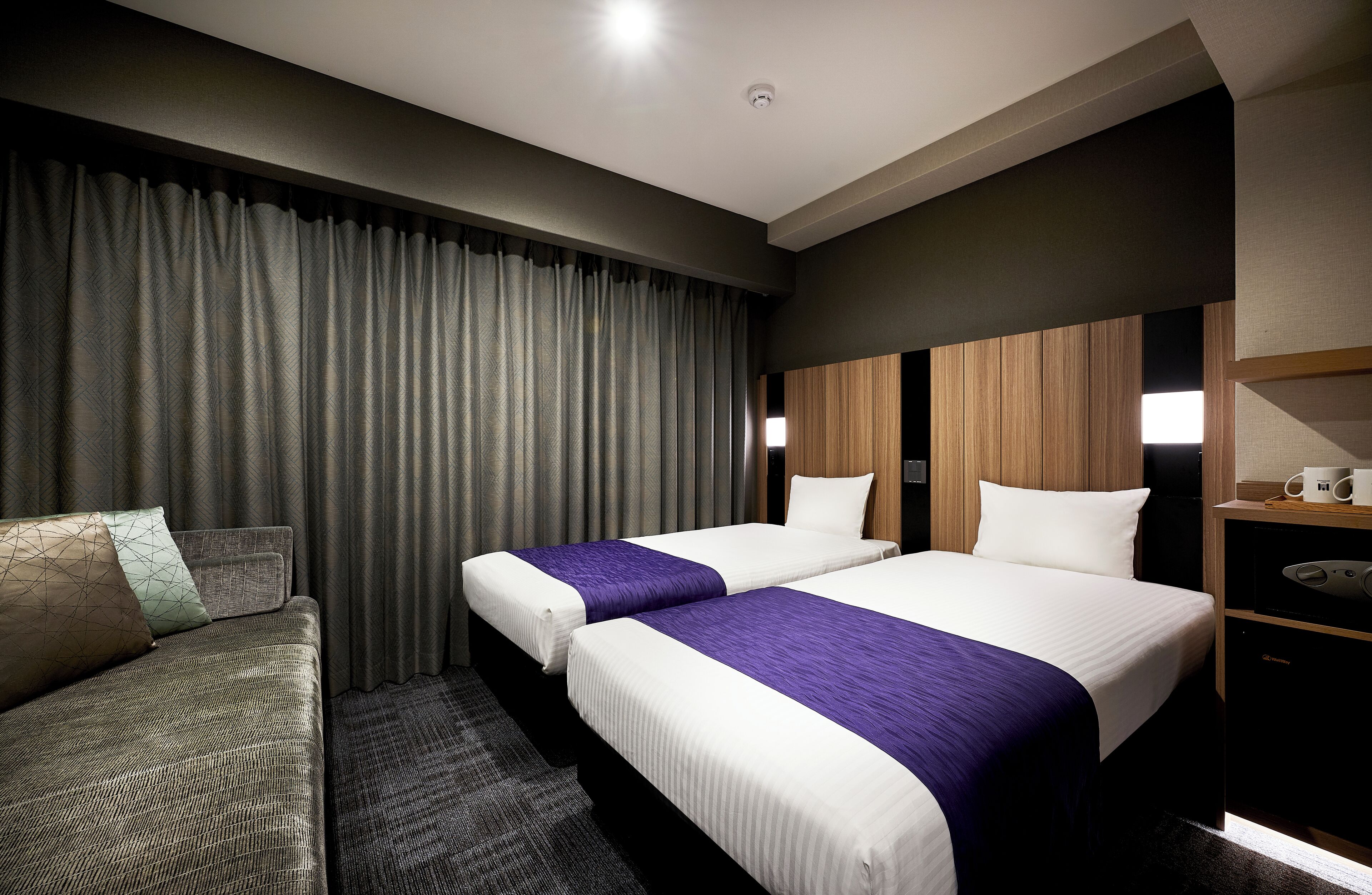 A hotel room with two beds, a sofa, and a wooden headboard.