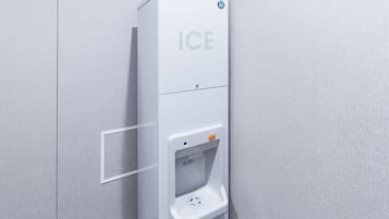 Un distributeur de glaçons blanc, avec le mot « GLACE » inscrit dessus, un bouton-poussoir et une étiquette d’avertissement.