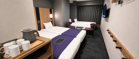 Habitación de hotel con dos camas, un escritorio con tetera, televisión y perchero.