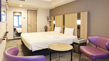 A hotel room with a large bed, a bedside table, a chair, a small round table, and a wardrobe.