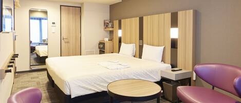 A hotel room with a large bed, a bedside table, a chair, a small round table, and a wardrobe.