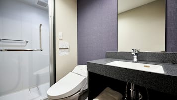 Un baño moderno con cabina de ducha de vidrio, inodoro blanco y tocador con lavamanos negro.