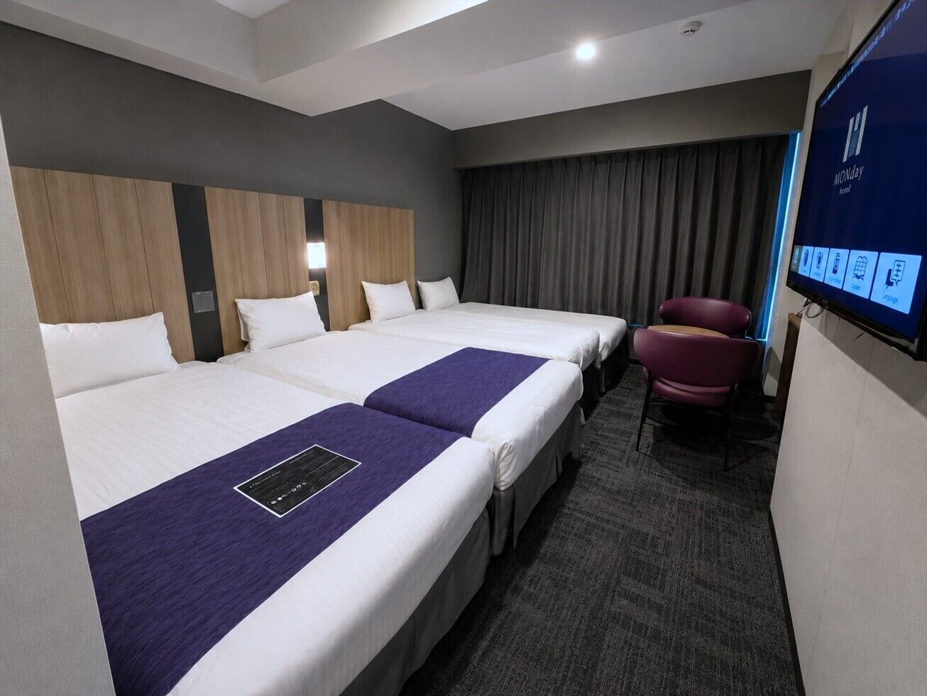 A hotel room with three beds, a flat-screen TV, a desk, and a chair.
