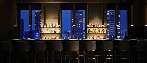 A bar area with multiple stools and a cityscape view through large windows.