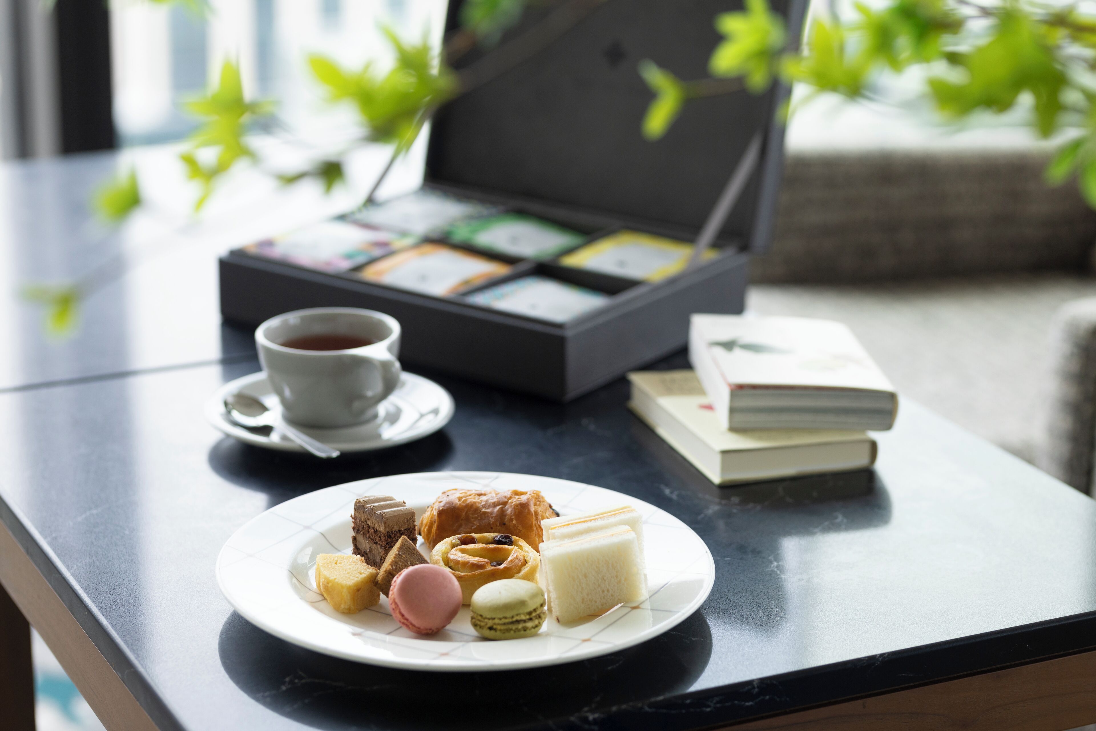 A table with a plate of pastries, a cup of coffee, and a tea box.