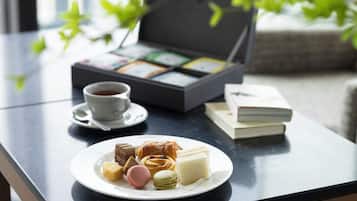 A table with a plate of pastries, a cup of coffee, and a tea box.
