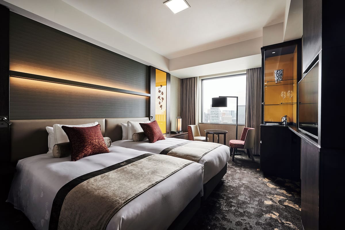 A hotel room with two beds, a desk, a chair, and a large window.