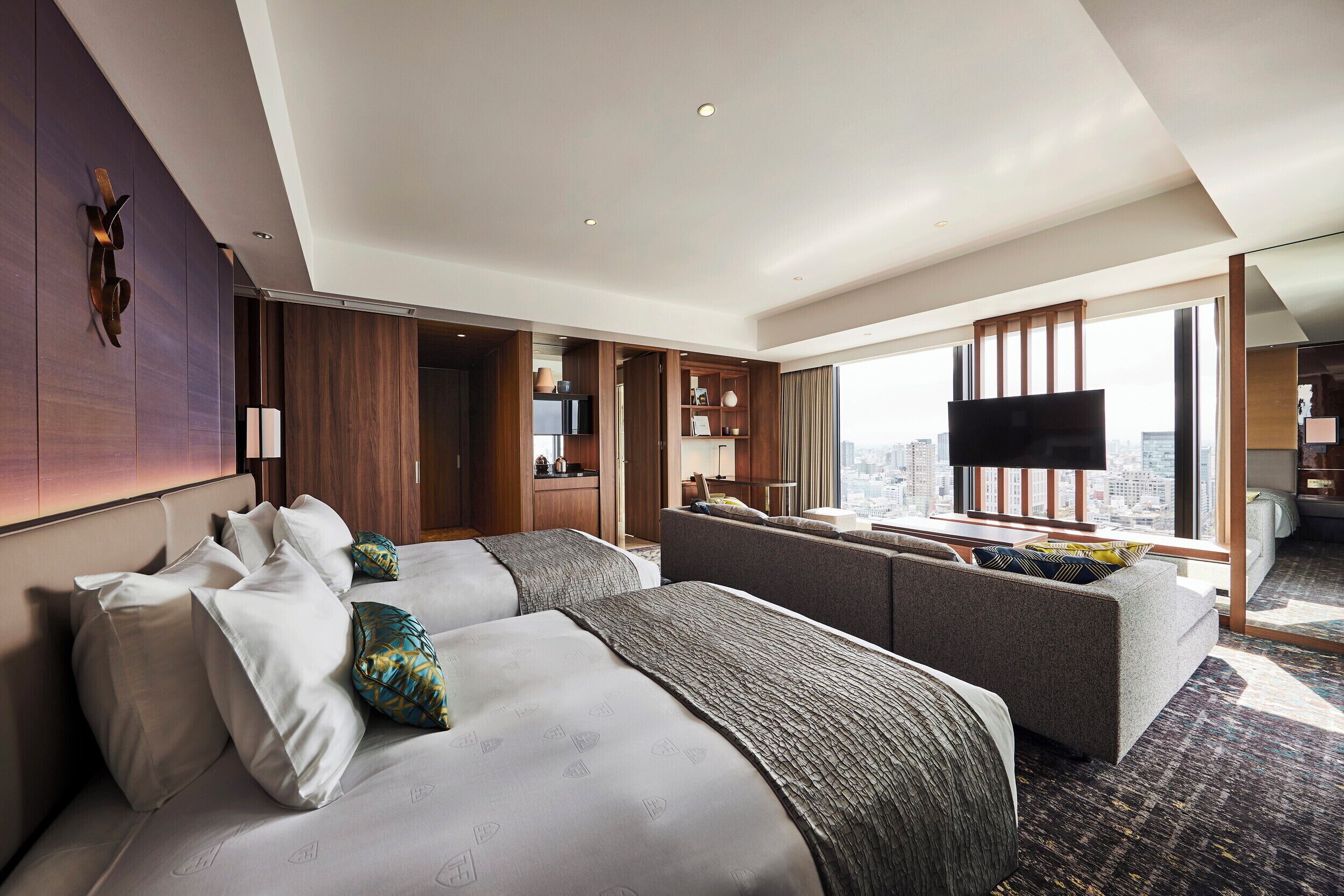A modern hotel room with a large bed, a sofa, a TV, and a city view.
