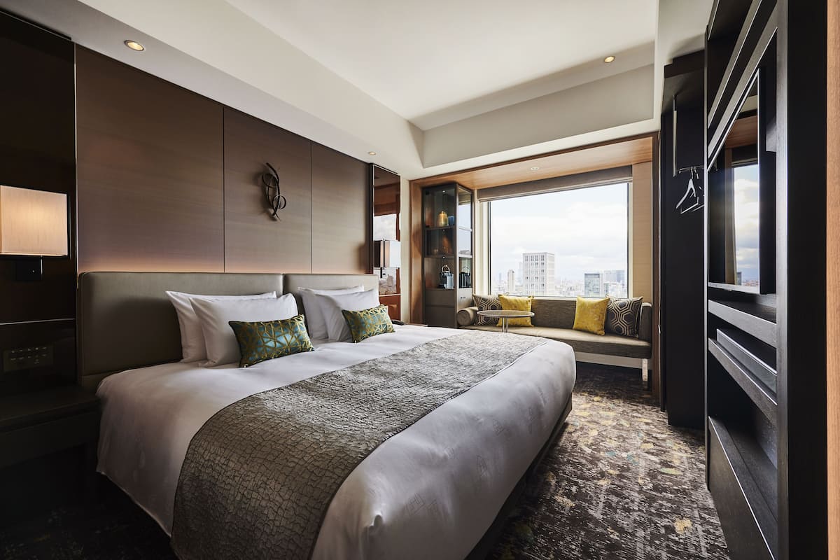 A modern hotel room with a large bed, a seating area with a view, and a wardrobe.