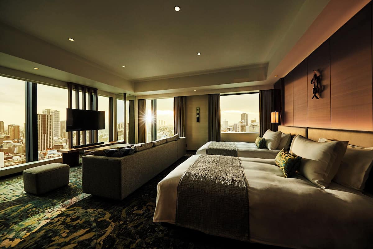 A hotel room with a large bed, a sofa, a TV, and a city view.