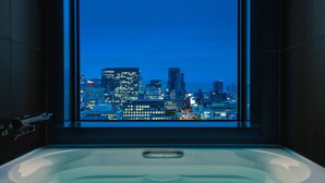 Un baño moderno con una bañera grande y vistas a la ciudad a través de un ventanal alto.