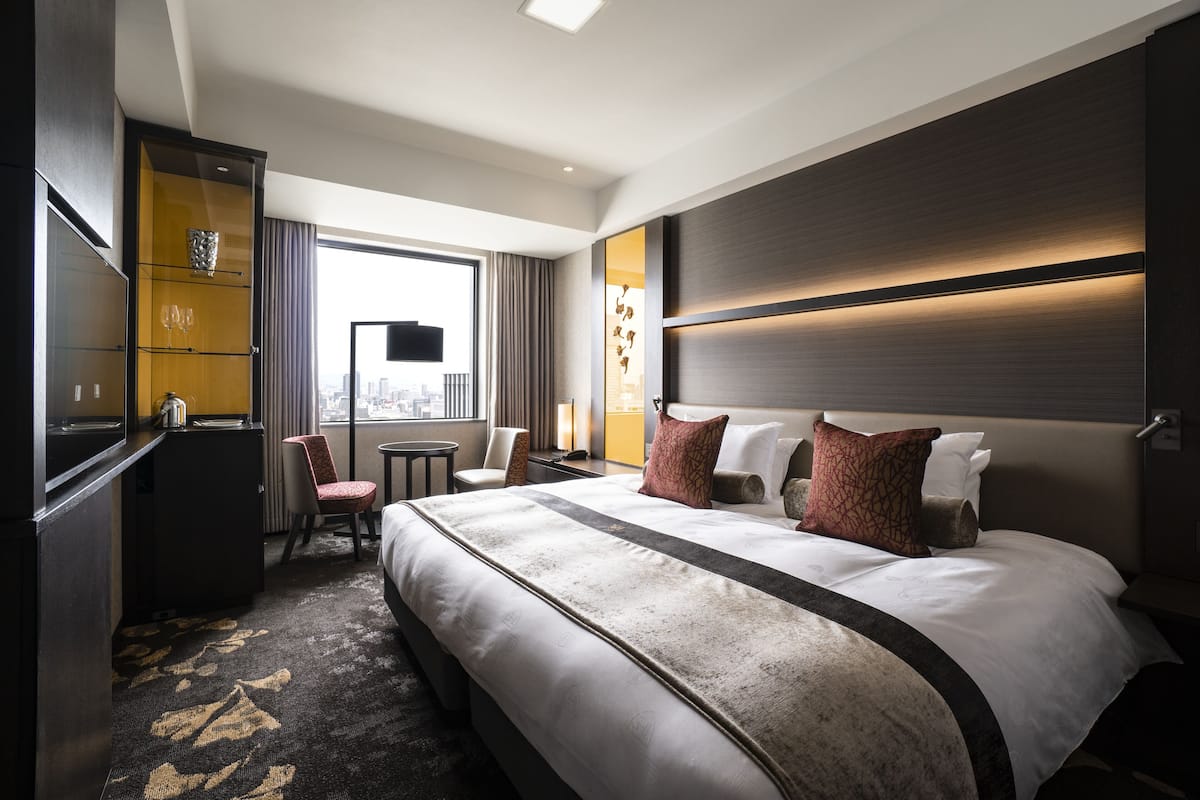 A hotel room with a large bed, a desk, a chair, and a view of the city.