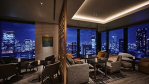 A modern living room with a city view, furnished with sofas, chairs, and a coffee table.