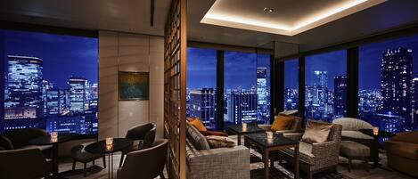 A modern living room with a city view, furnished with sofas, chairs, and a coffee table.
