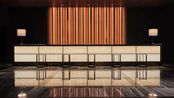 A reception area with a polished marble floor, a reception desk with a vertical light panel, and two lamps on either side.