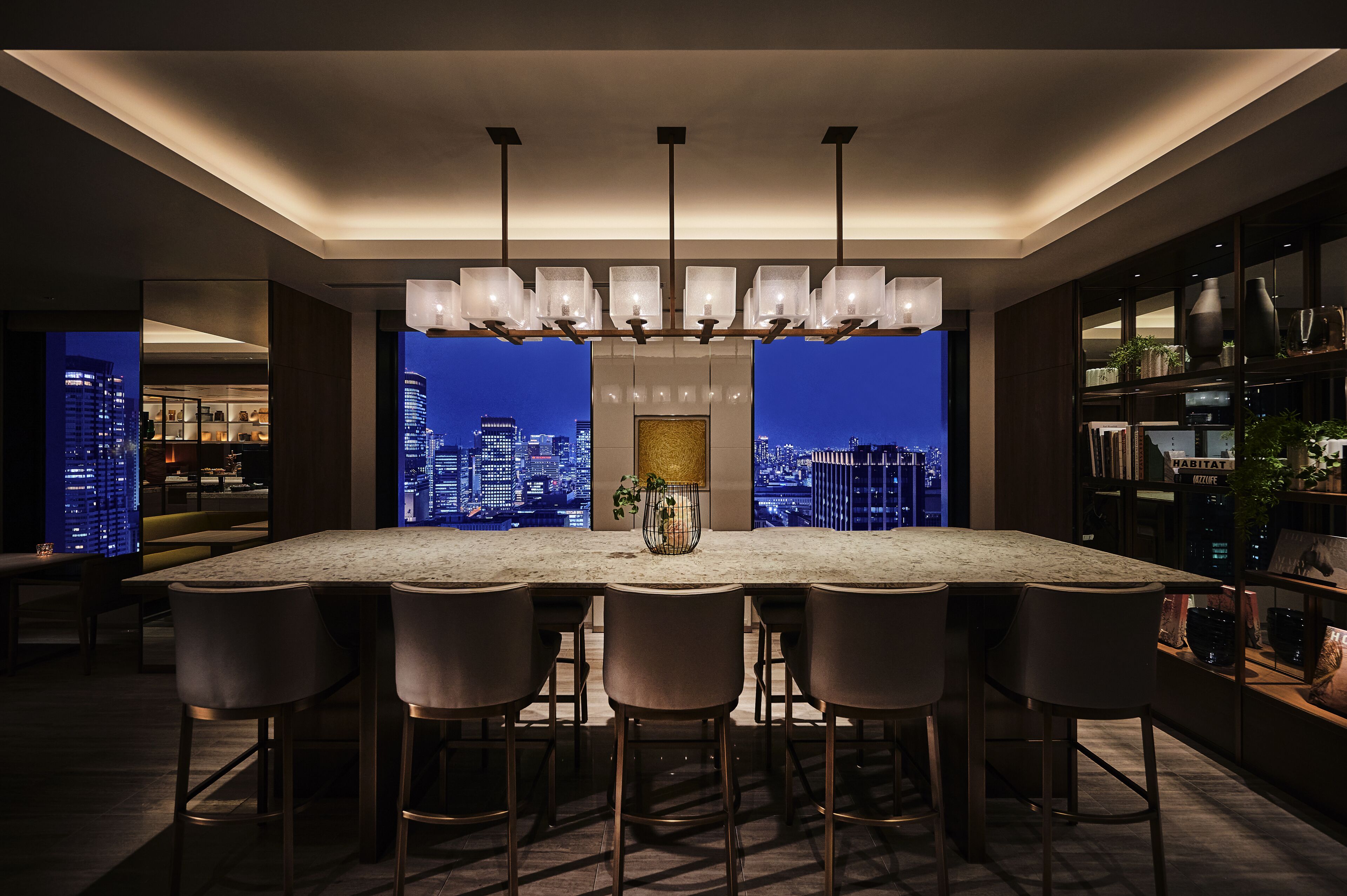 Une cuisine moderne dotée d’un grand îlot central, de tabourets de bar, de luminaires suspendus et offrant une vue sur la ville.