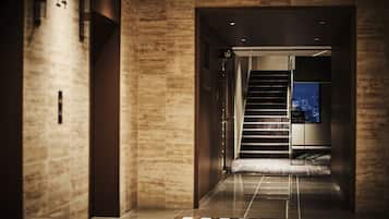 A modern hotel hallway with a marble wall, a digital display, and a staircase leading to the upper floors.