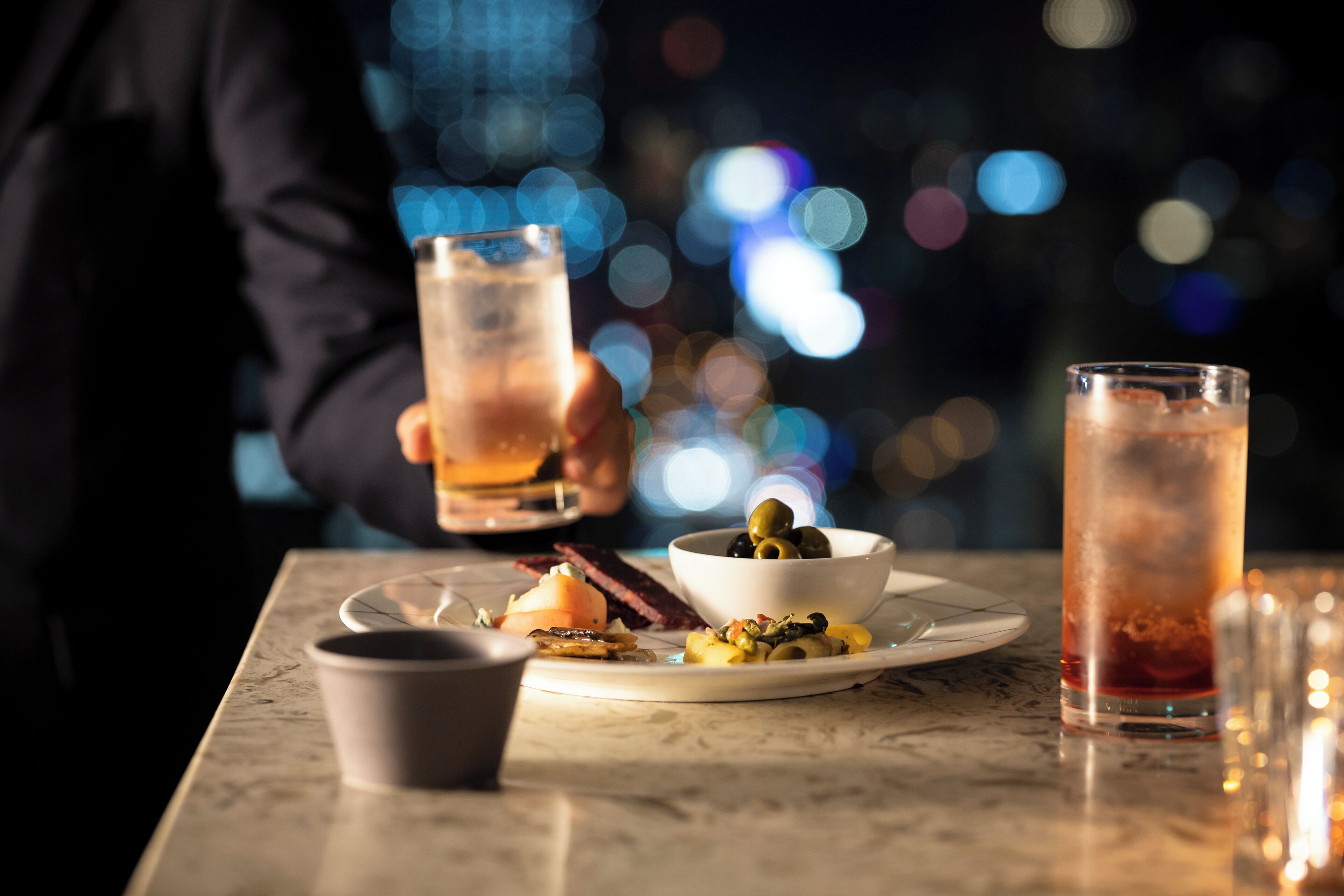 A table with a glass of iced tea, a bowl of olives, and a plate with food.