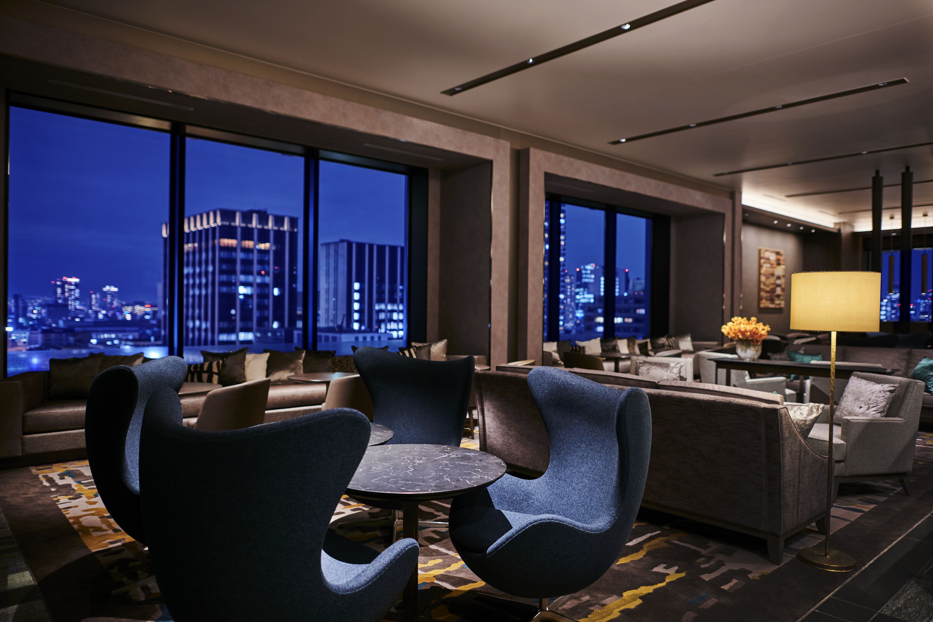 A modern hotel lobby with a city view, comfortable seating, and a well-lit ambiance.