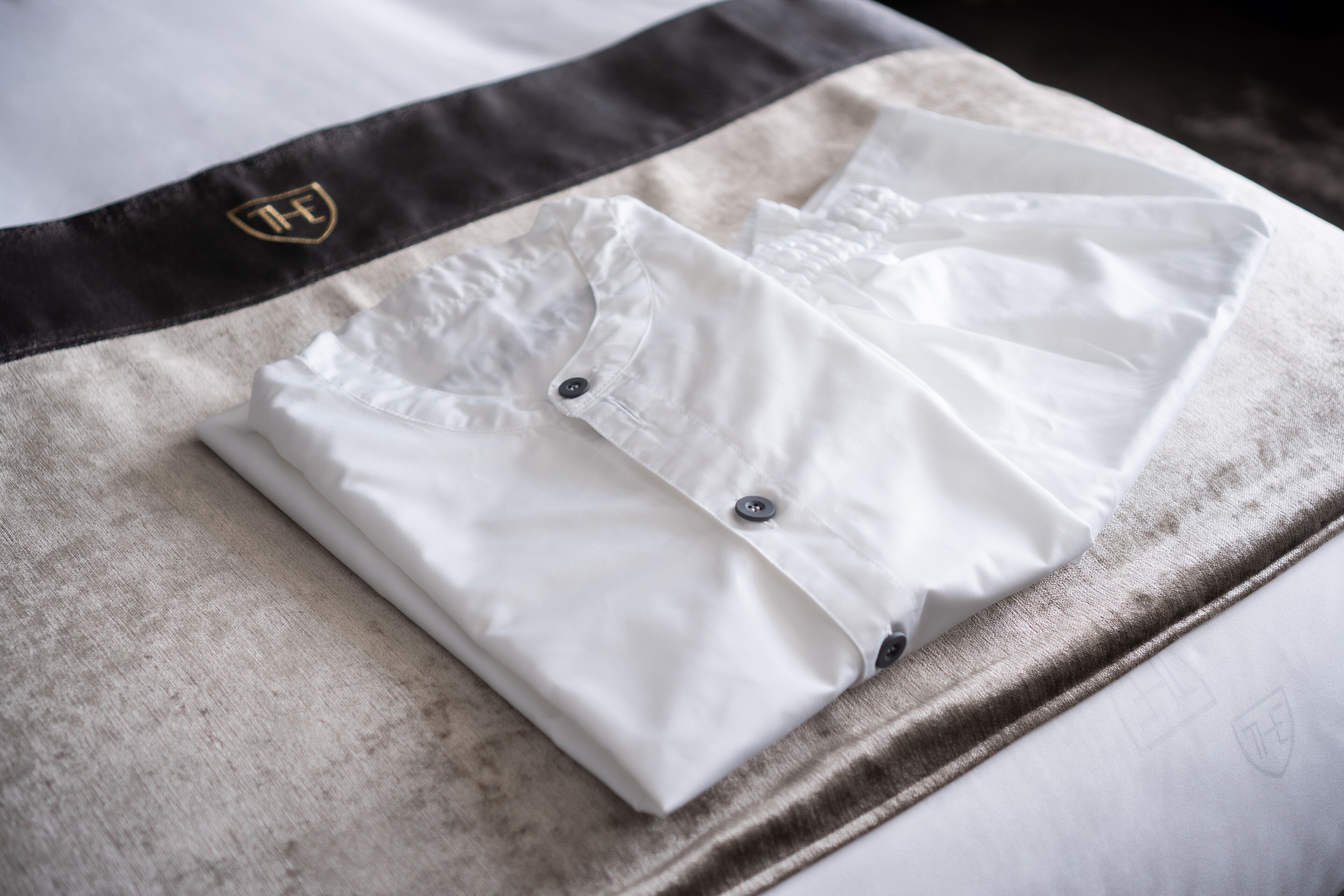 Una camisa blanca doblada con un logotipo en el puño, sobre una superficie de tela texturizada.