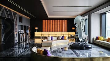 Un hall d’hôtel moderne avec un espace salon aux lignes courbes, un grand miroir et un mur orné de motifs.