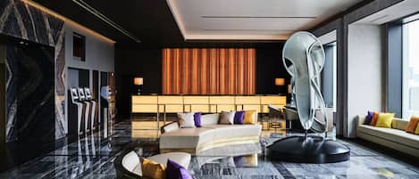 A modern hotel lobby with a curved seating area, a large mirror, and a patterned wall.