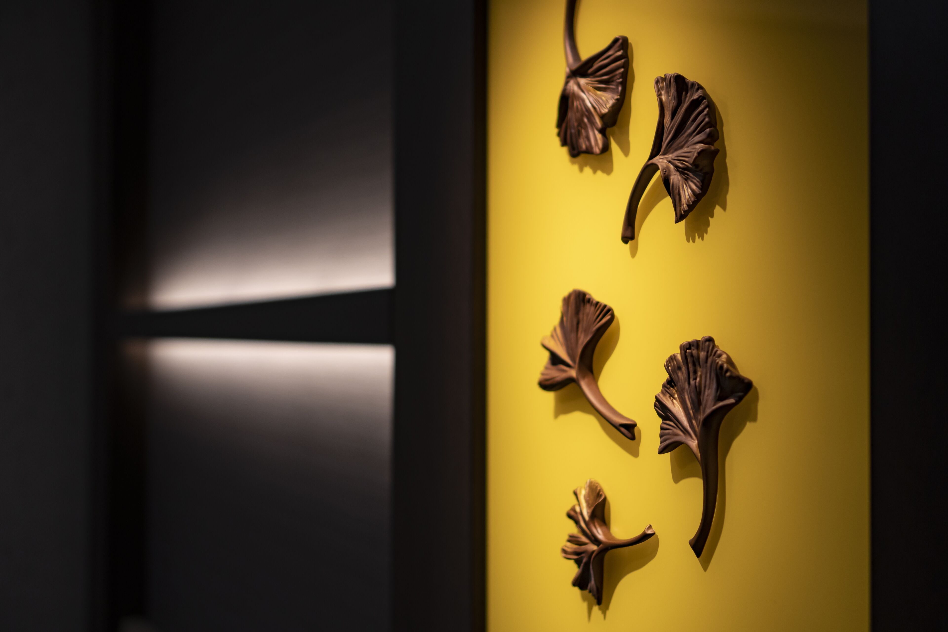 A room with a yellow wall and a dark floor. There are four decorative wall pieces on the wall.