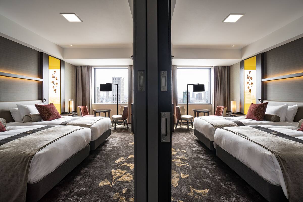 A mirrored hotel room with two beds, a city view, and modern decor.