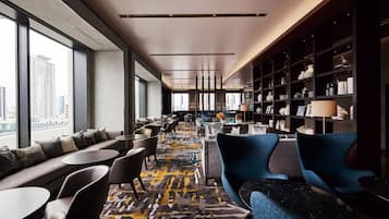 A modern hotel lobby with a long seating area, a bookshelf, and a view of the city.