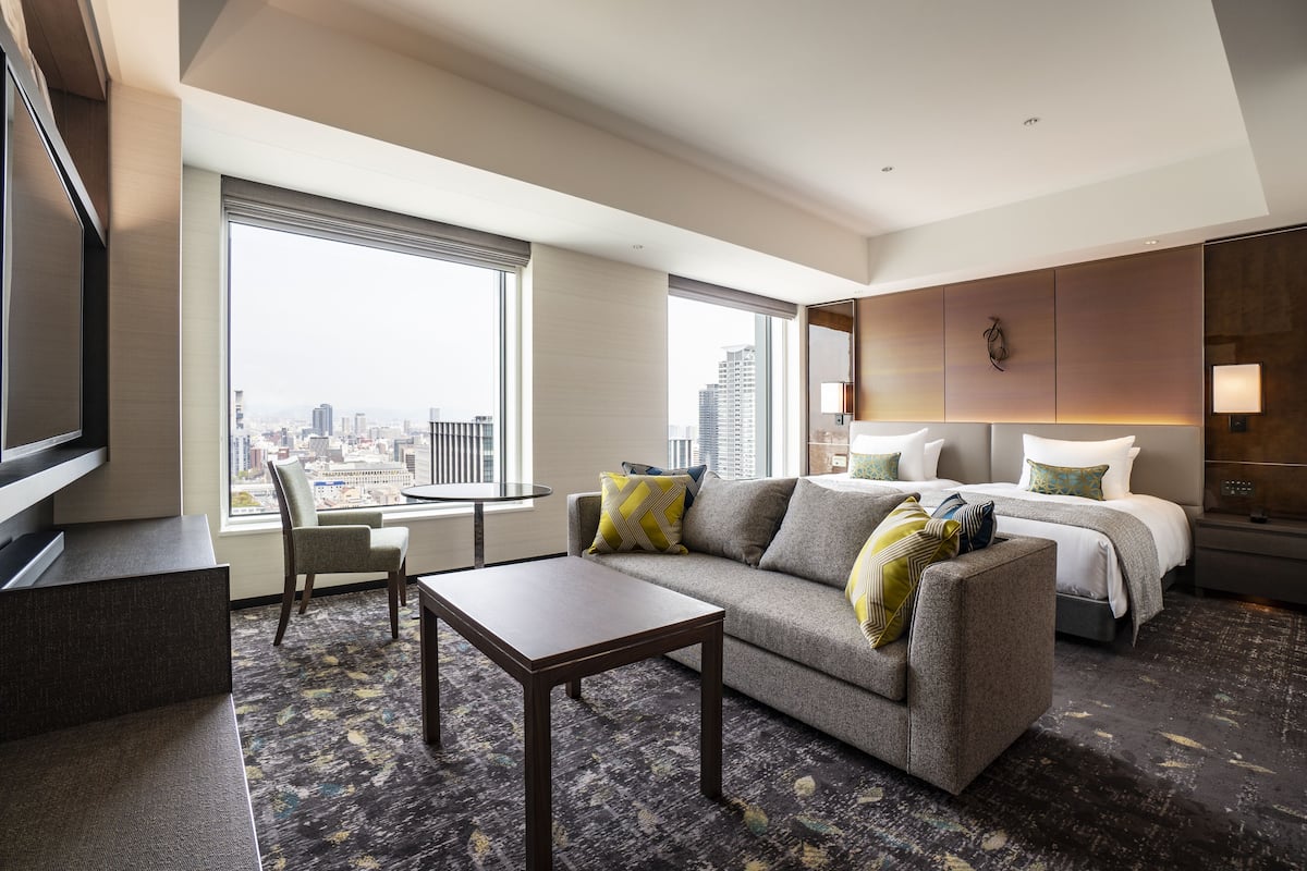 A hotel room with a large bed, a sofa, a small table, and a TV.