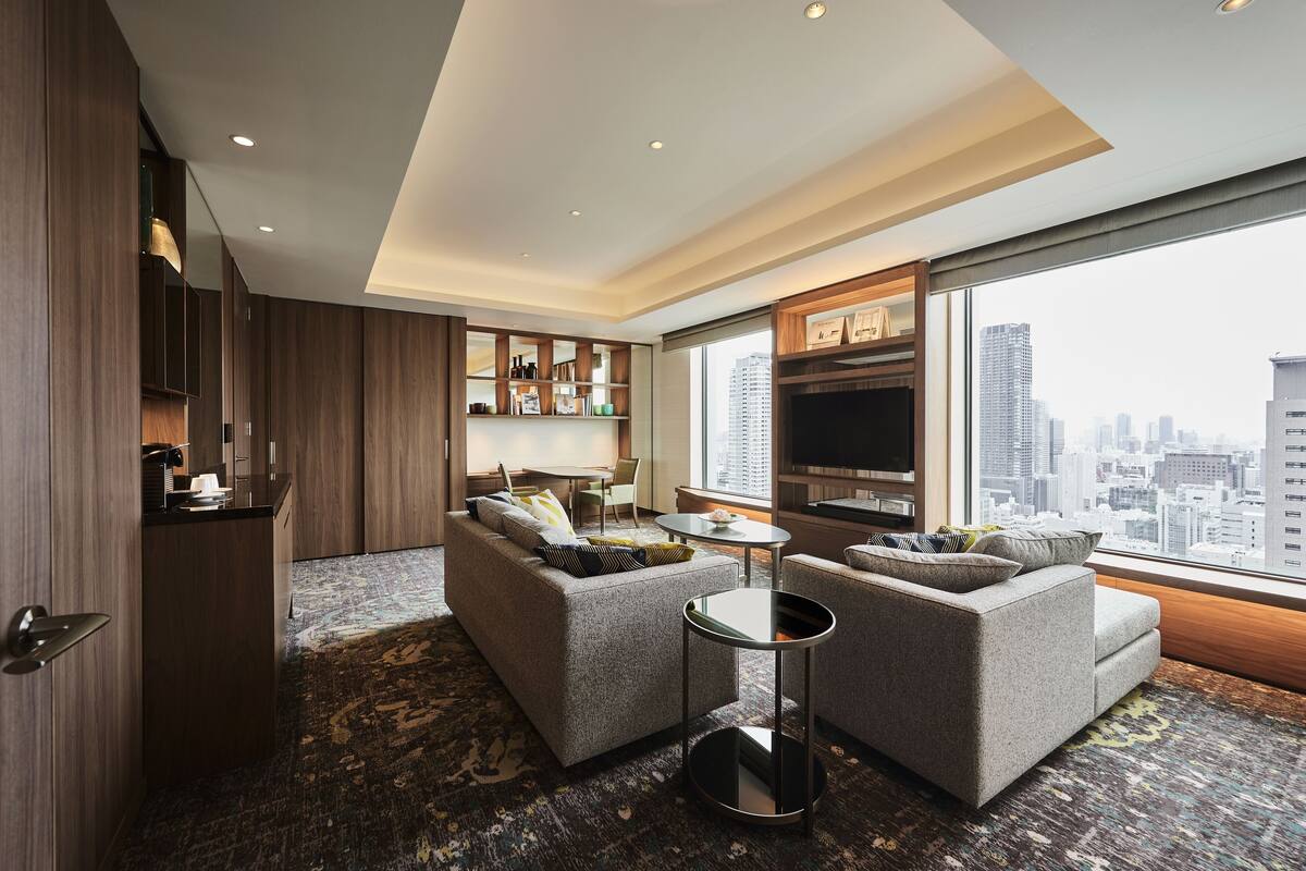 A modern hotel room with a city view, a sofa set, a small table, and a TV.