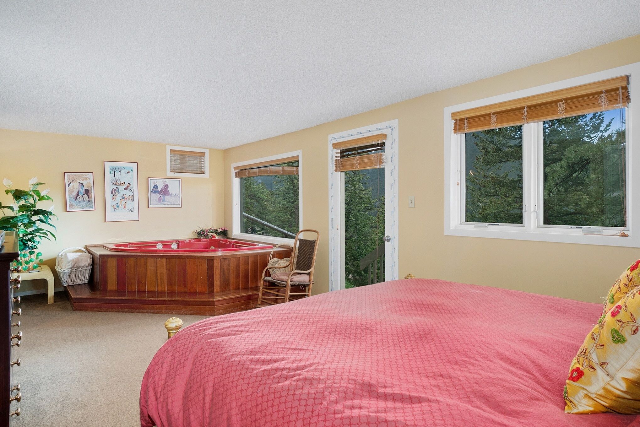 A bedroom with a large bed, a wooden bathtub, a chair, and a window with a view of trees.