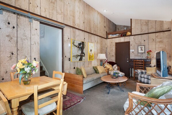 A cozy living room with a wooden wall, a sofa, a dining table with chairs, and a television. - Deering Crest -- Ev #3249 3 Bedroom Condo by RedAwning (Estes Park)
