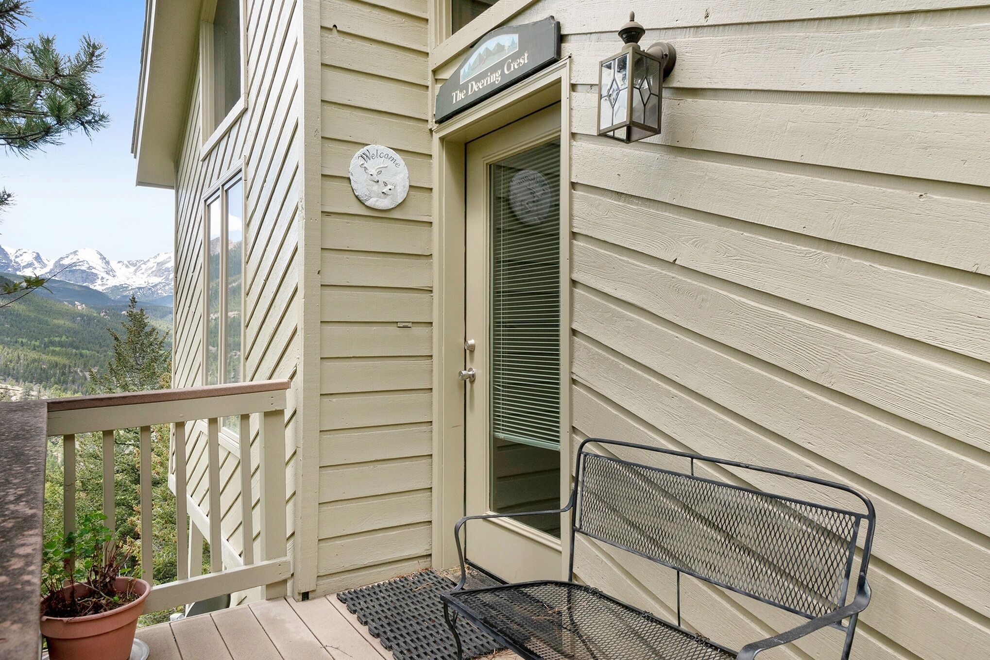 A balcony with a metal bench, a welcome sign, and a door with blinds.