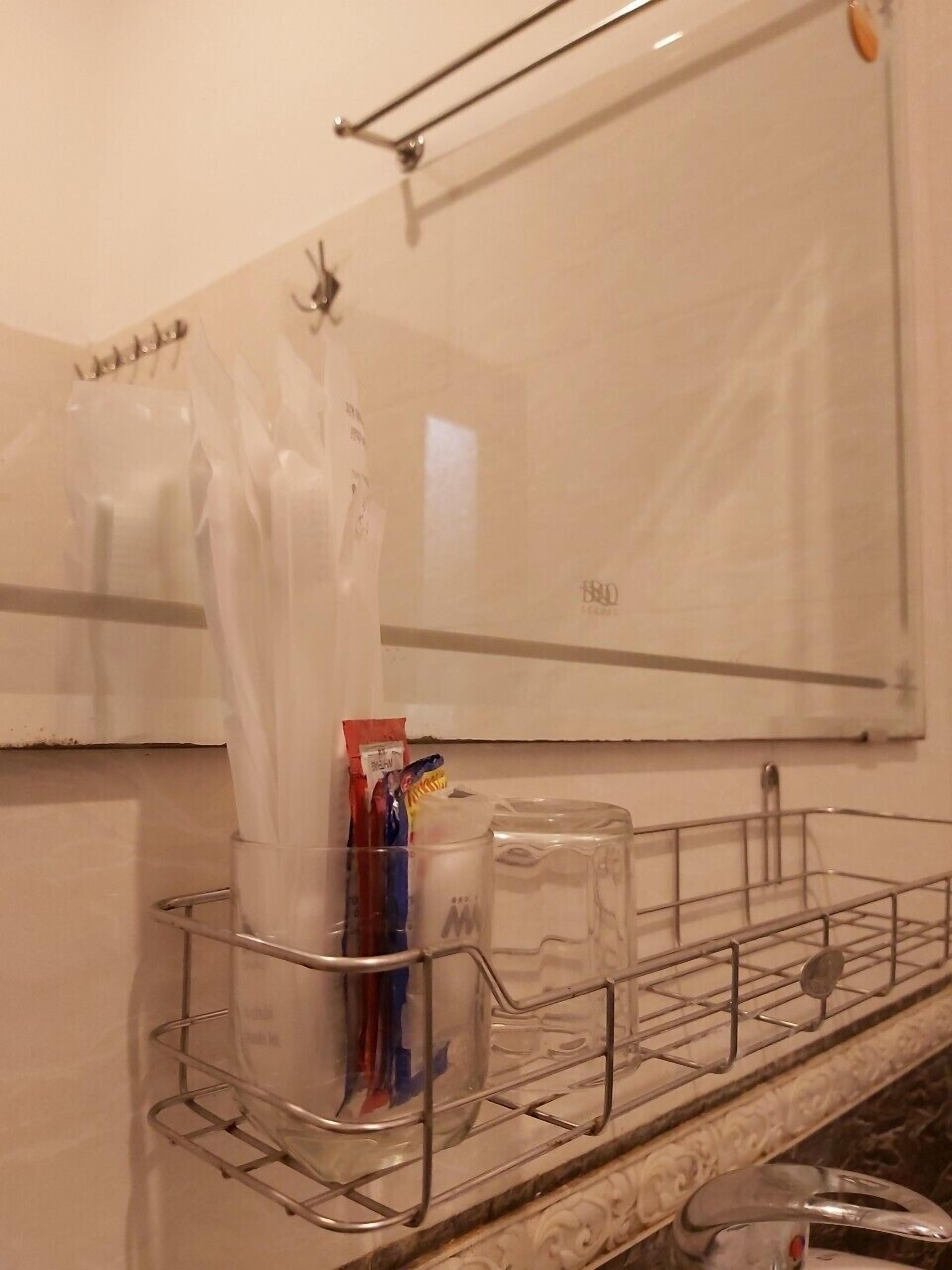 Un bagno con specchio, porta asciugamani, ripiano in vetro con articoli da toilette e piano in marmo.
