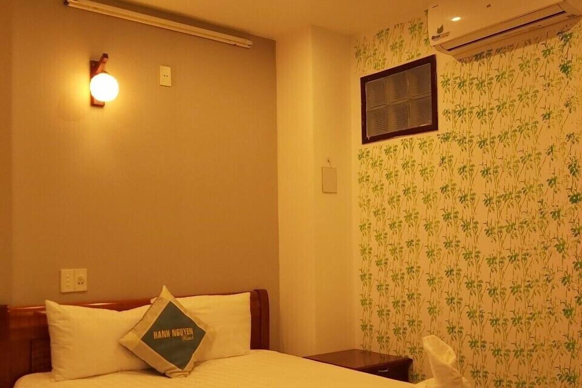Une chambre d’hôtel avec un lit, un climatiseur fixé au mur, une applique murale et un papier peint à motifs.