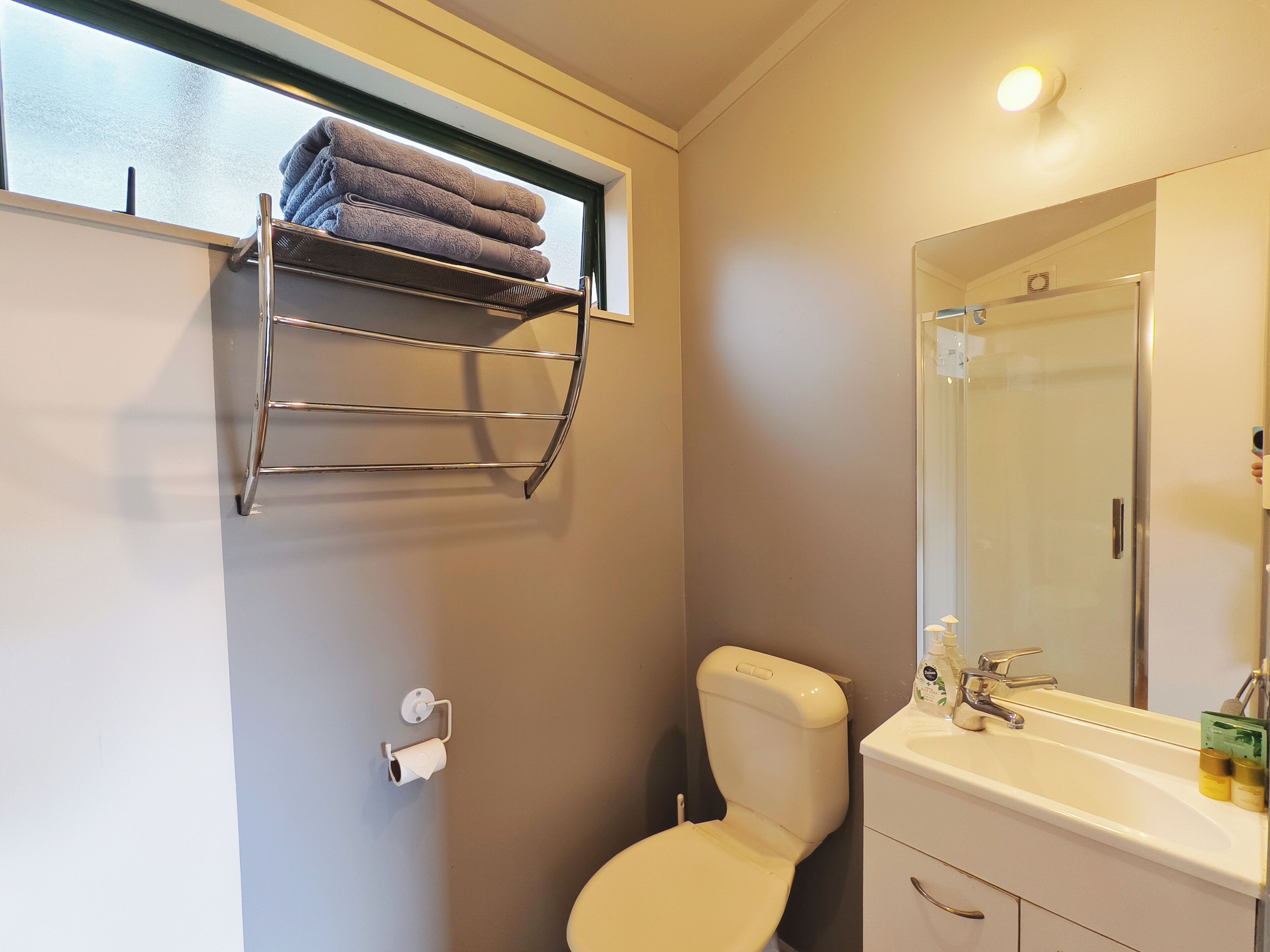 A bathroom with a toilet, sink, mirror, towel rack, and a window.