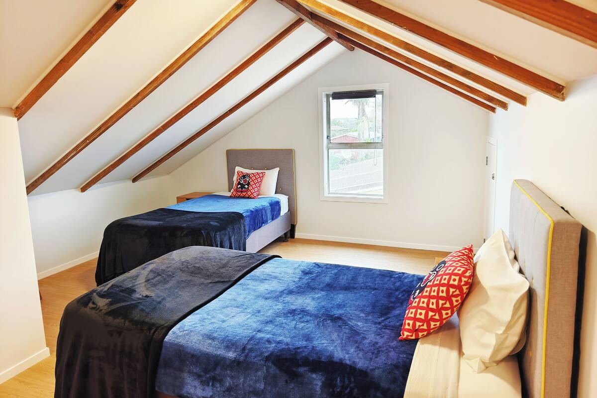 Un dormitorio con dos camas, una ventana y vigas de madera inclinadas.