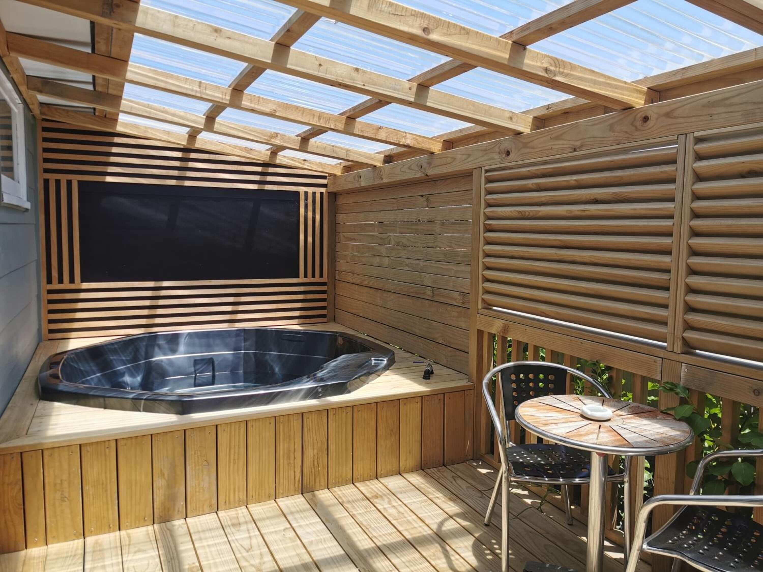 Une terrasse en bois avec un jacuzzi, une table et des chaises.