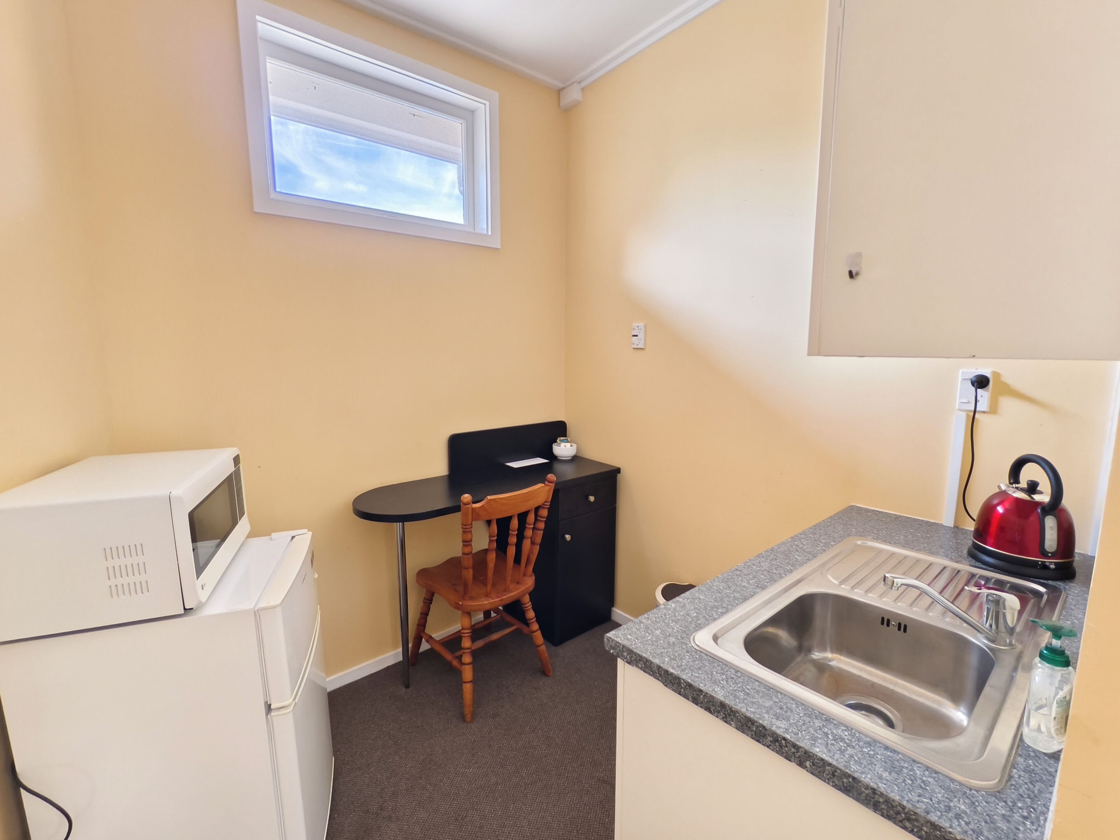 A compact kitchenette with a microwave, a small table with a chair, a kettle, and a sink.