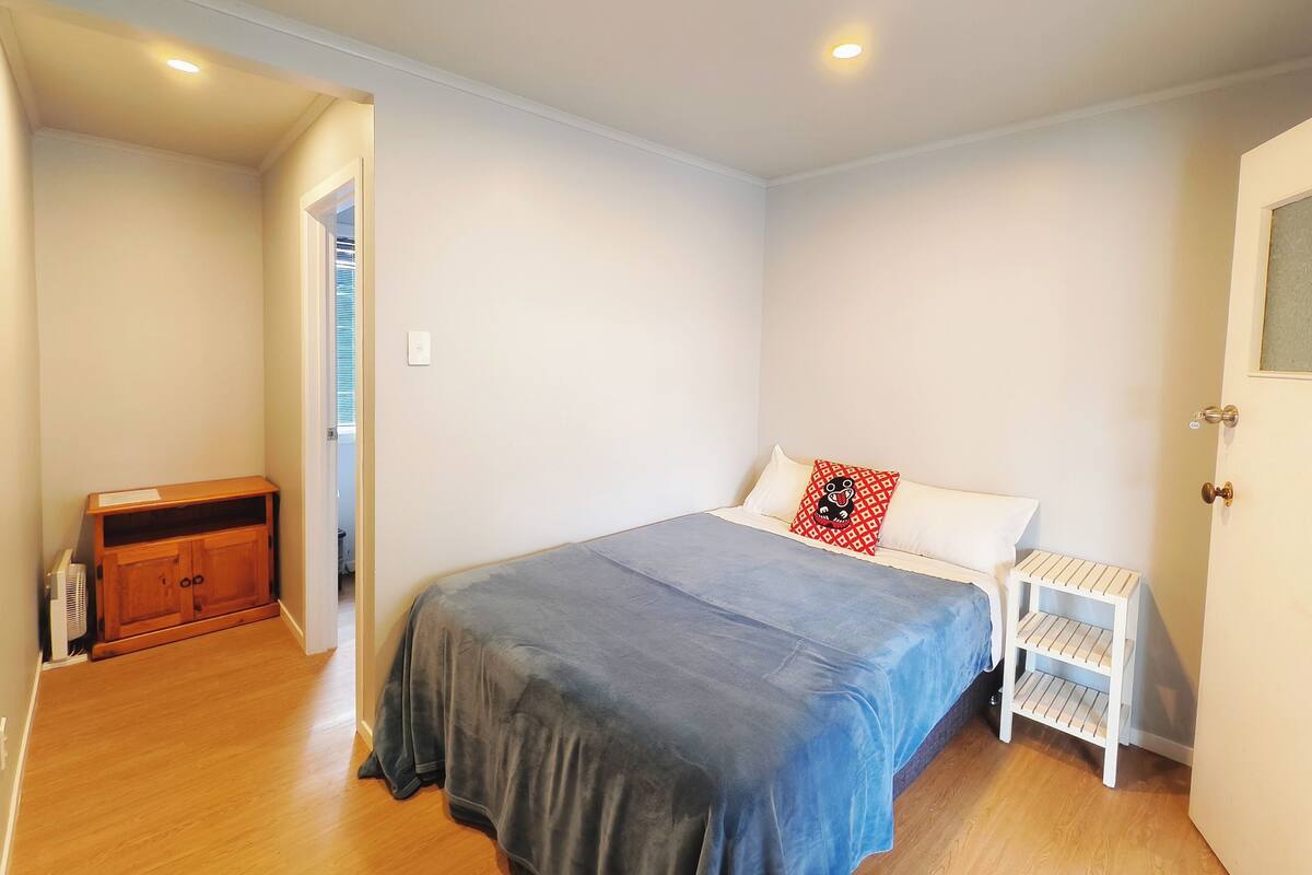 Un dormitorio con cama, un armario de madera, una mesita de noche blanca y una puerta.