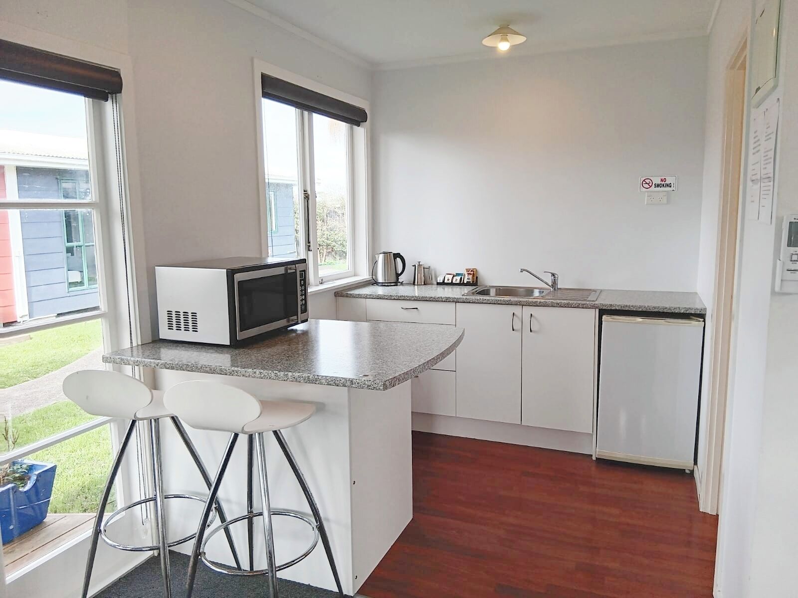 A kitchen with white cabinets, a microwave, a sink, and a bar stool.