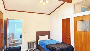 A bedroom with a bed, a radiator, a chair, and a wooden door.