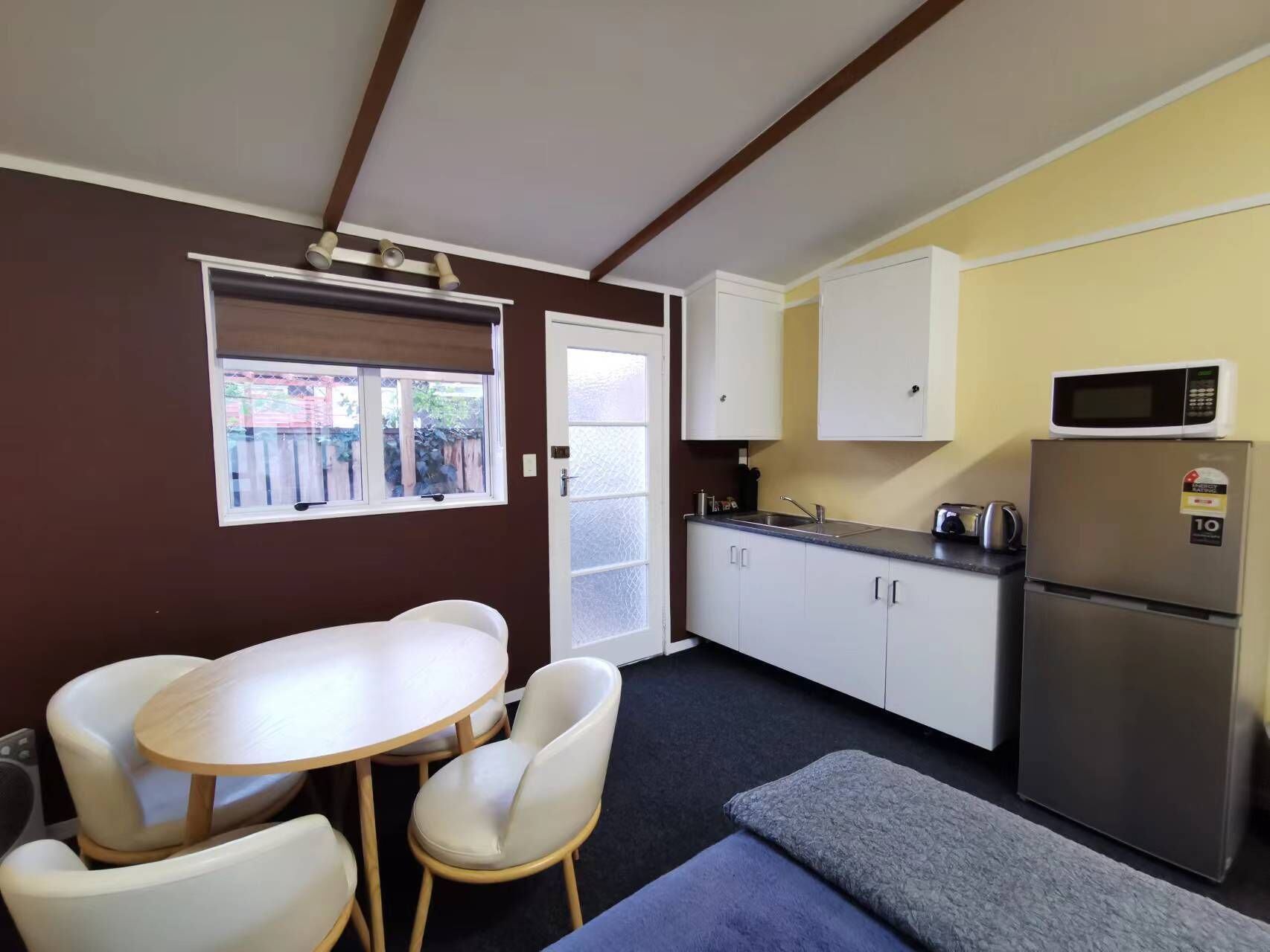 Una kitchenette compacta con microondas, refrigerador y pileta. Hay un pequeño comedor con mesa y sillas.