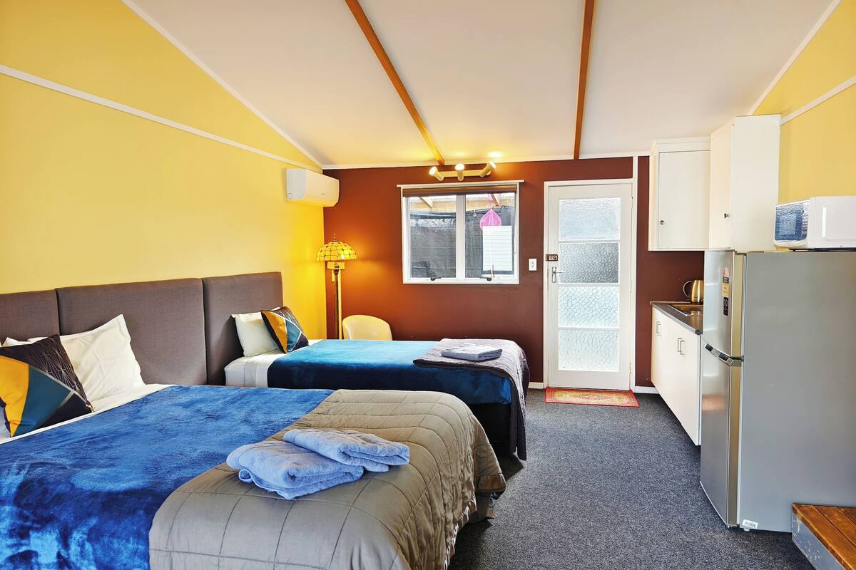 Habitación de hotel con dos camas, un escritorio, un refrigerador y una ventana.