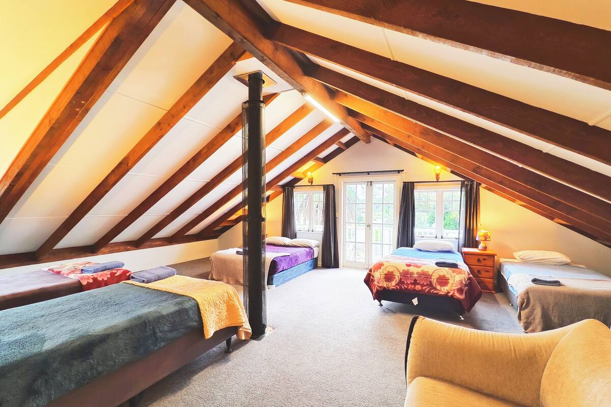 Un dormitorio en el ático con techo inclinado, vigas de madera y tres camas.