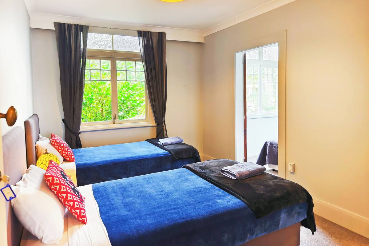Una habitación con dos camas, una ventana con cortinas, una puerta y una lámpara en el techo.