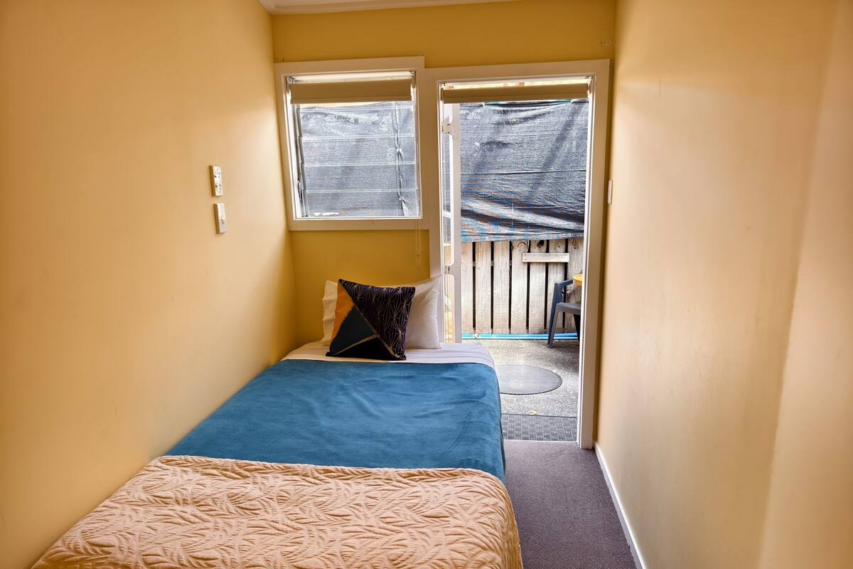 Habitación estrecha con cama, ventana y puerta que da a un espacio exterior.