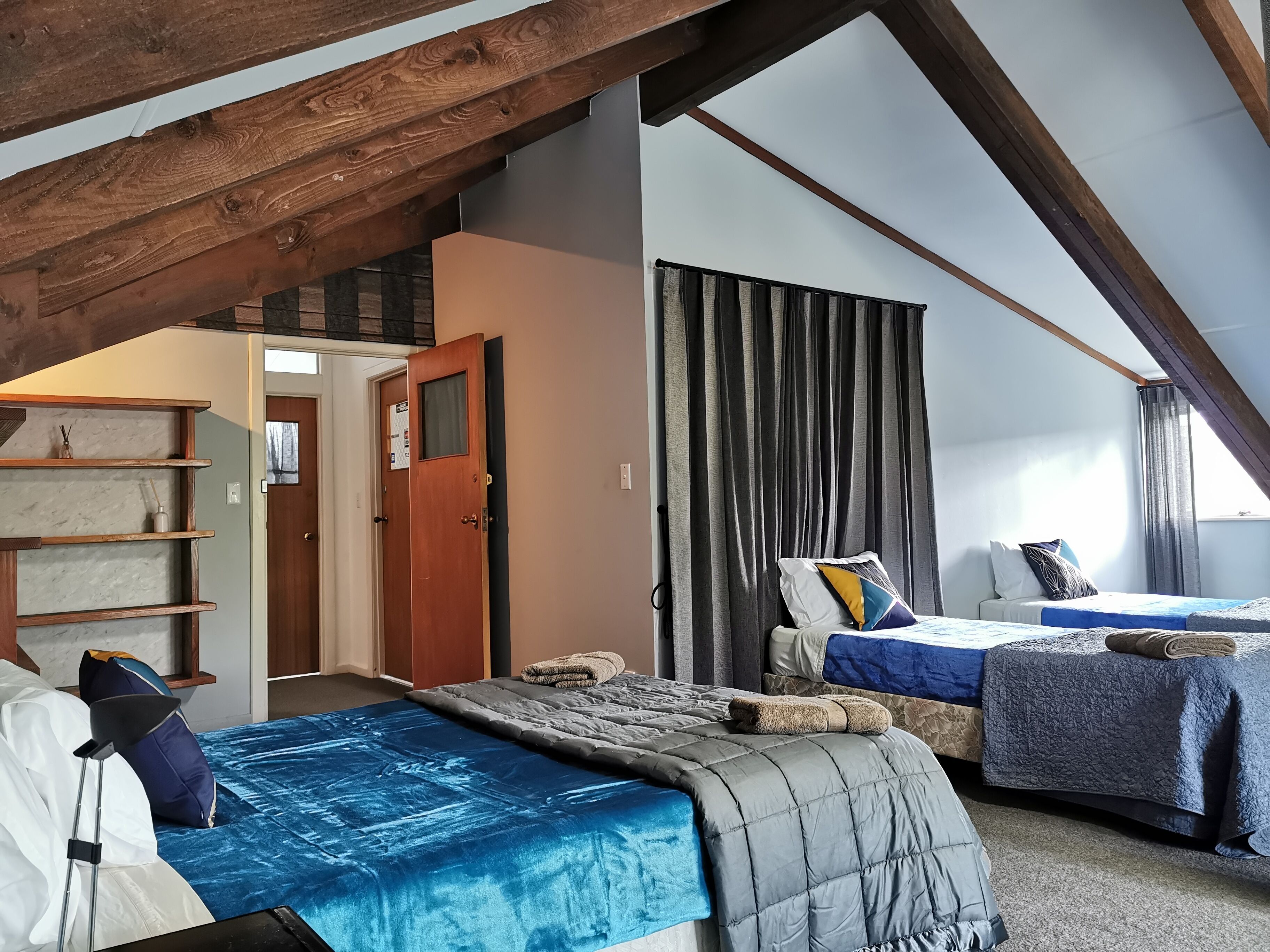 A bedroom with two beds, wooden beams, a door, and a shelf with toiletries.